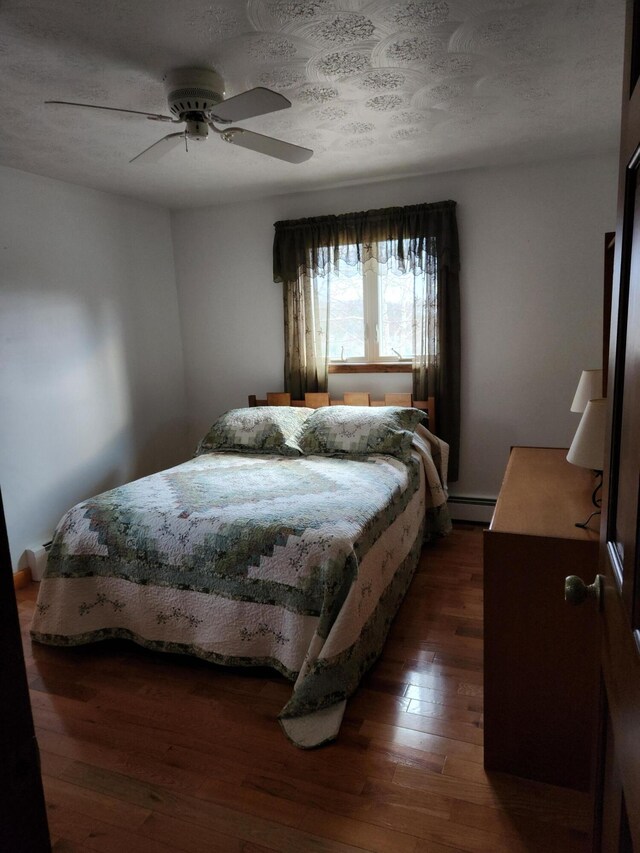 bedroom with ceiling fan, a baseboard heating unit, a textured ceiling, and dark hardwood / wood-style floors