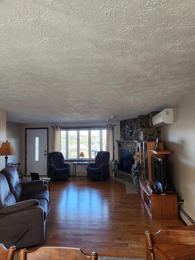 living area featuring a baseboard heating unit, a stone fireplace, wood finished floors, a textured ceiling, and a wall mounted AC