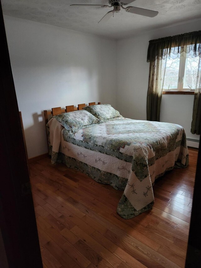 bedroom with a baseboard heating unit, dark wood-type flooring, and ceiling fan