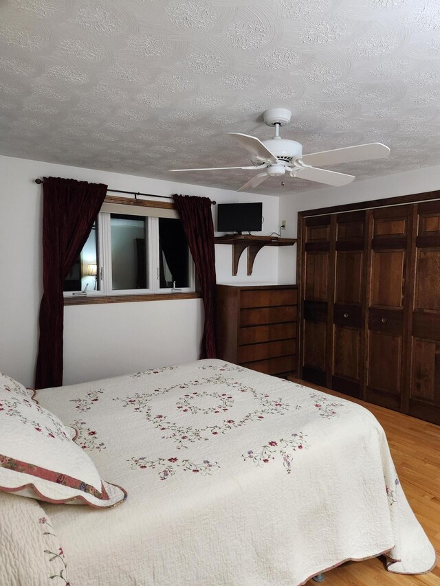 bedroom with light hardwood / wood-style flooring, a textured ceiling, a closet, and ceiling fan