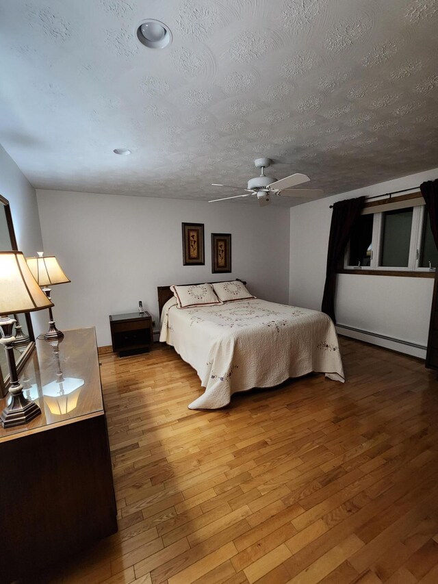 bedroom featuring hardwood / wood-style floors, a textured ceiling, a baseboard radiator, and ceiling fan