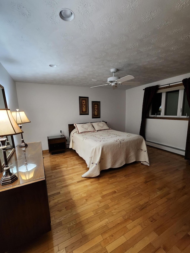 bedroom with a baseboard heating unit, a textured ceiling, hardwood / wood-style floors, and a ceiling fan