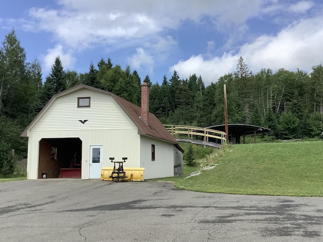 exterior space with a forest view, a gambrel roof, a chimney, an outdoor structure, and a garage