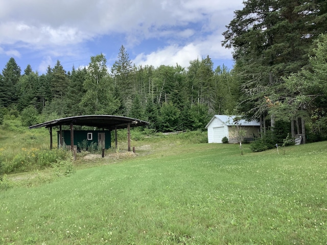 view of yard featuring an outbuilding, a view of trees, and a carport