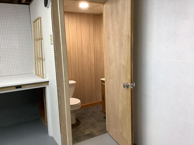 bathroom featuring tile patterned floors, wooden walls, and toilet