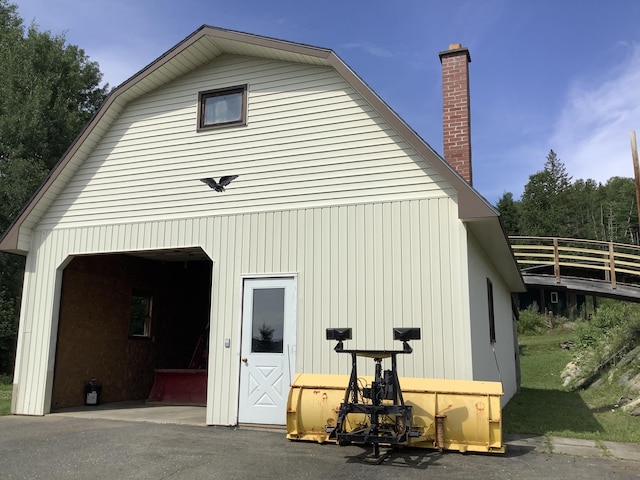 exterior space with an outdoor structure, a garage, a gambrel roof, and a chimney