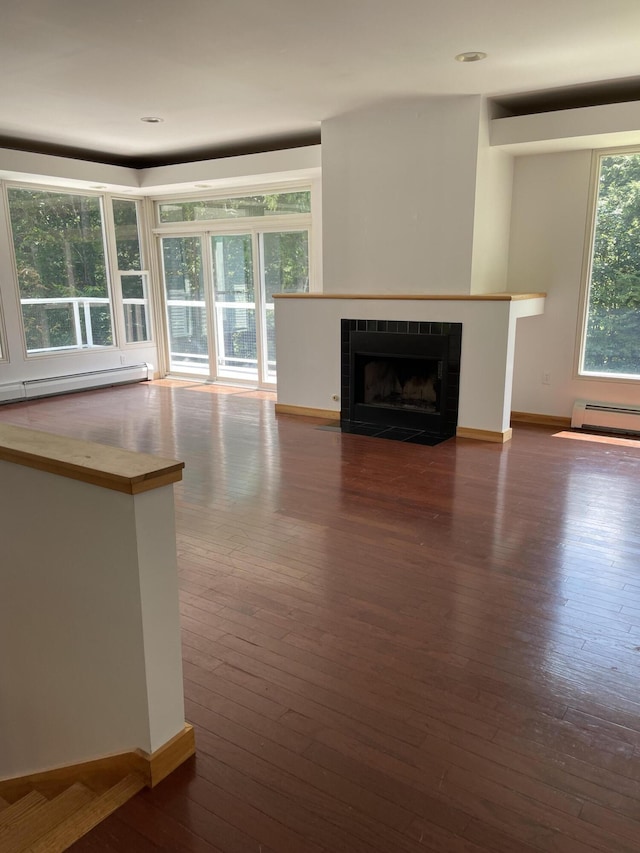 unfurnished living room with baseboard heating, dark hardwood / wood-style flooring, and a tile fireplace