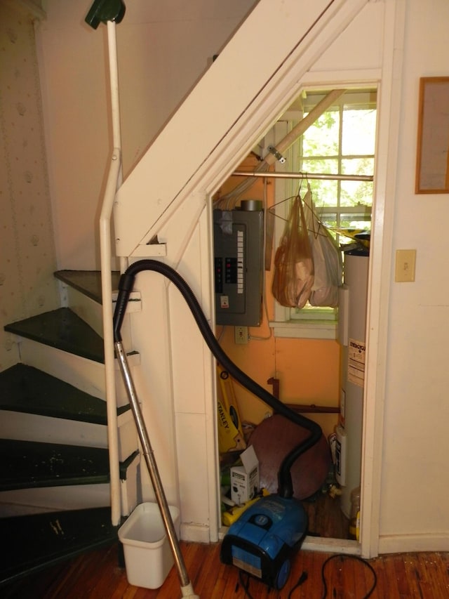 stairs featuring hardwood / wood-style floors, water heater, and electric panel