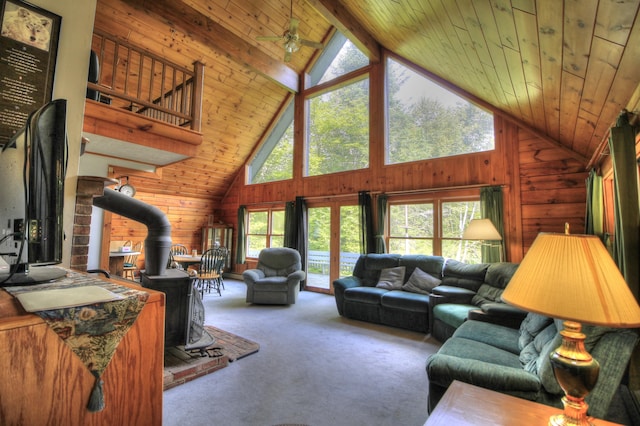 living room with beam ceiling, a wood stove, high vaulted ceiling, wood walls, and carpet