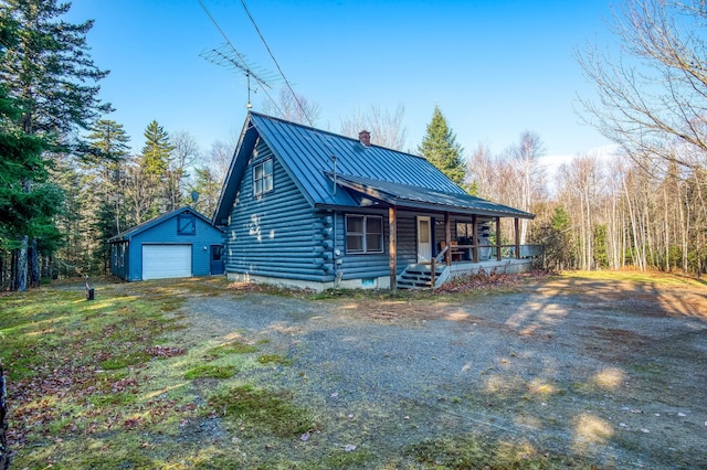 cabin with metal roof, covered porch, an outdoor structure, driveway, and a standing seam roof