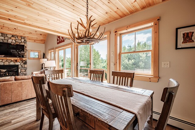 dining area featuring plenty of natural light, a stone fireplace, light wood-type flooring, and a chandelier