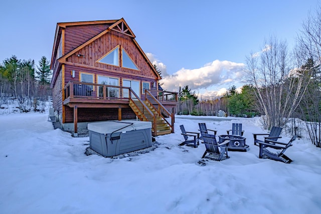 snow covered house featuring a hot tub, an outdoor fire pit, and a wooden deck