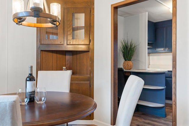 dining area featuring dark wood-type flooring, wooden walls, and a notable chandelier