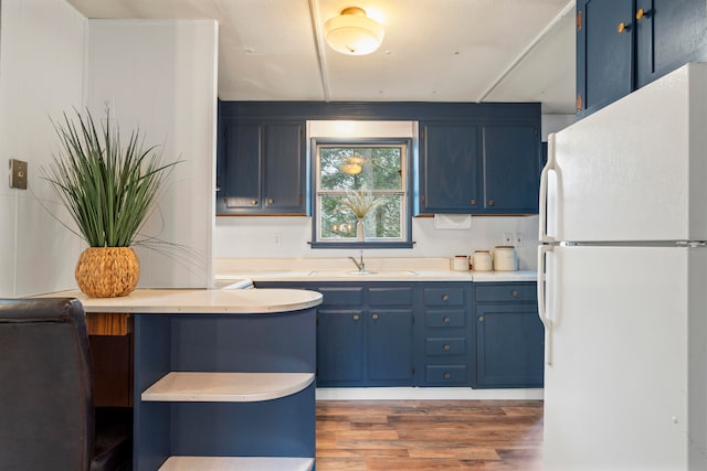 kitchen with wood-type flooring, white fridge, sink, and blue cabinets