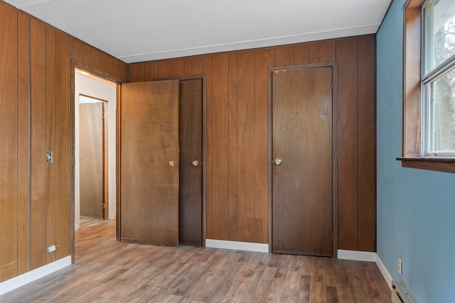 unfurnished bedroom featuring wood walls, light hardwood / wood-style flooring, and a baseboard heating unit