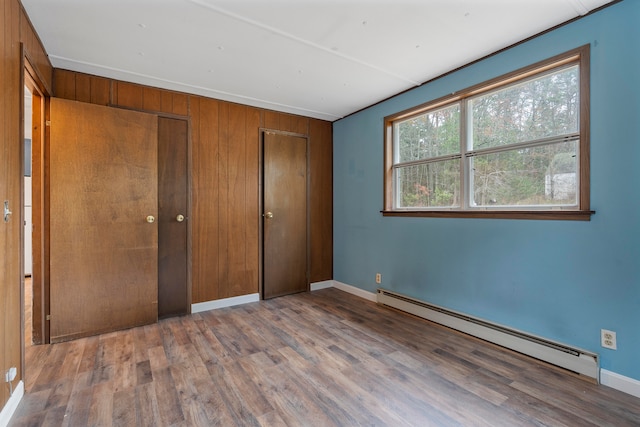 unfurnished bedroom with hardwood / wood-style flooring, wooden walls, and baseboard heating