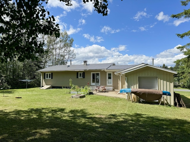 back of house with a chimney, metal roof, a lawn, and a patio