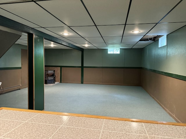 basement featuring a wood stove, a baseboard radiator, and a drop ceiling