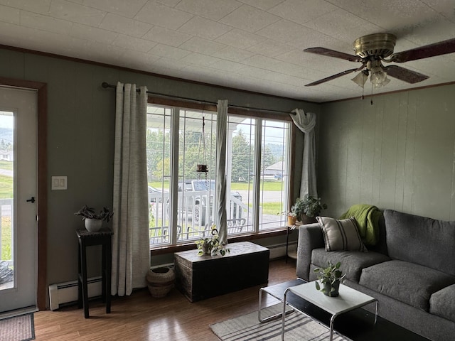 living room featuring a ceiling fan, a baseboard heating unit, wood finished floors, and ornamental molding