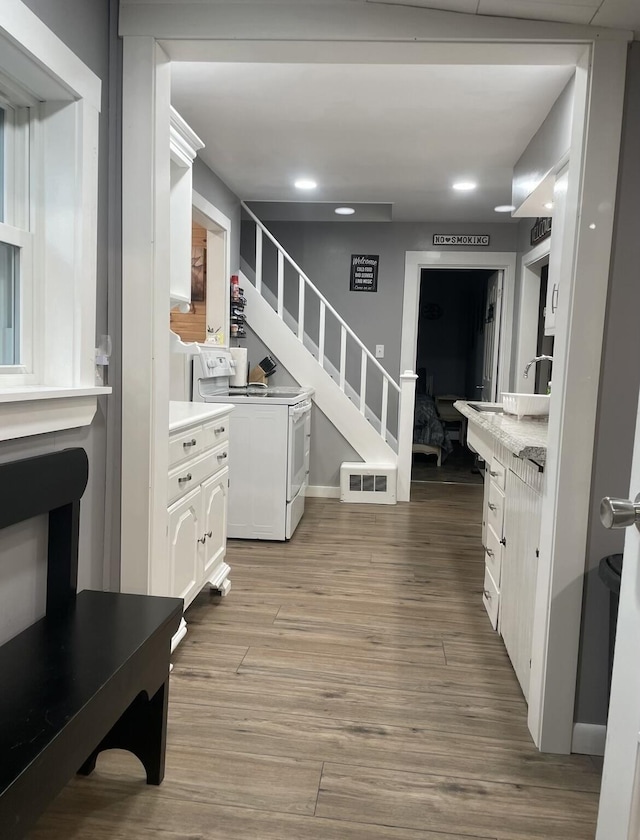 interior space featuring visible vents, baseboards, stairs, light wood finished floors, and white electric range oven