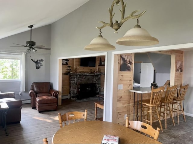 dining space featuring a fireplace, a baseboard heating unit, a ceiling fan, wood finished floors, and high vaulted ceiling