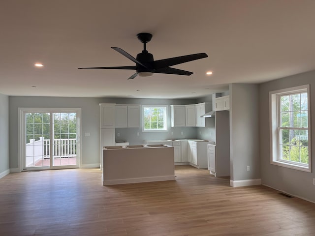 kitchen with white cabinetry, a center island, ceiling fan, light hardwood / wood-style floors, and wall chimney range hood