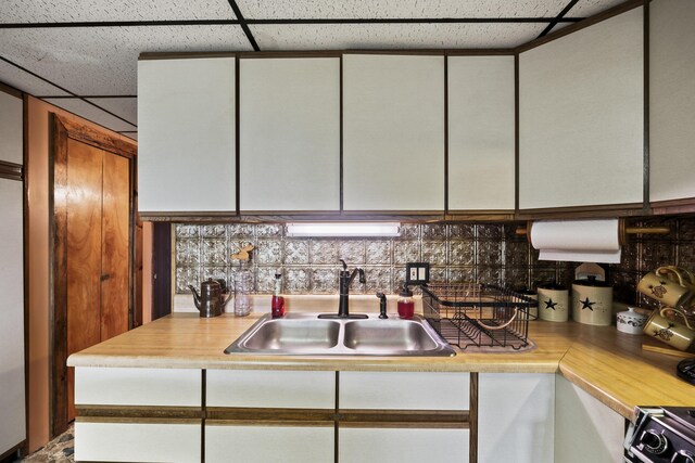 kitchen with backsplash, white cabinetry, and sink