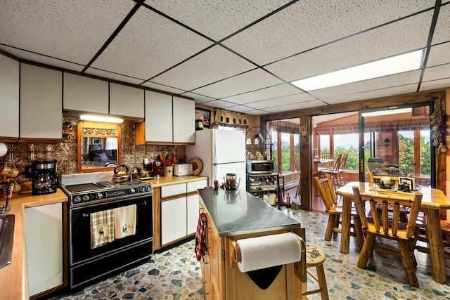 kitchen featuring black range with electric stovetop, white cabinetry, a drop ceiling, white refrigerator, and backsplash