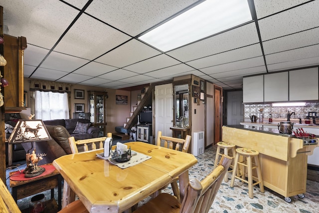 dining area featuring a bar, stairs, and a drop ceiling