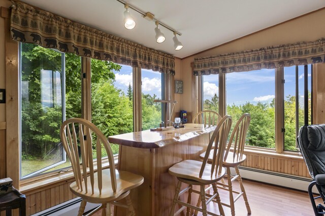 dining room with a baseboard heating unit, lofted ceiling, bar, and light hardwood / wood-style flooring