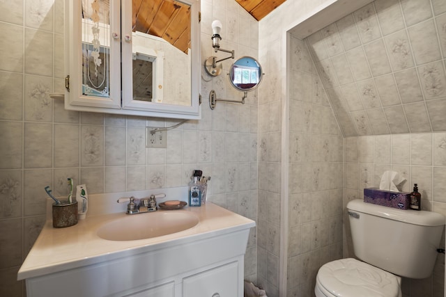 bathroom with wooden ceiling, vaulted ceiling, toilet, vanity, and tile walls