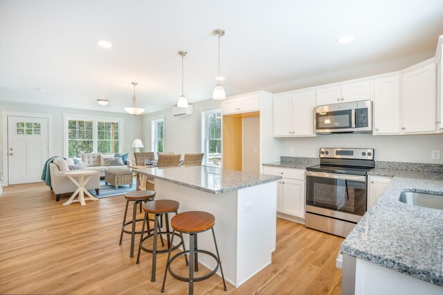 kitchen with stainless steel appliances, white cabinetry, light wood-type flooring, light stone countertops, and hanging light fixtures