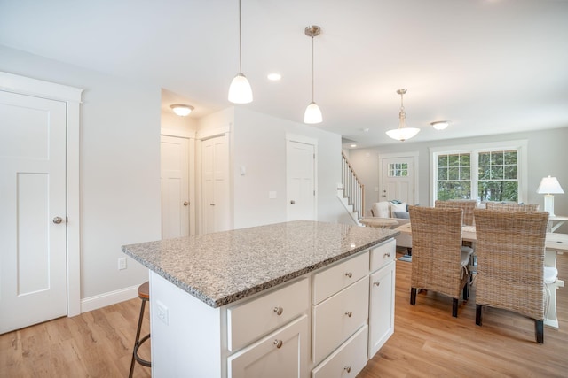 kitchen with white cabinetry, light hardwood / wood-style flooring, light stone counters, and decorative light fixtures