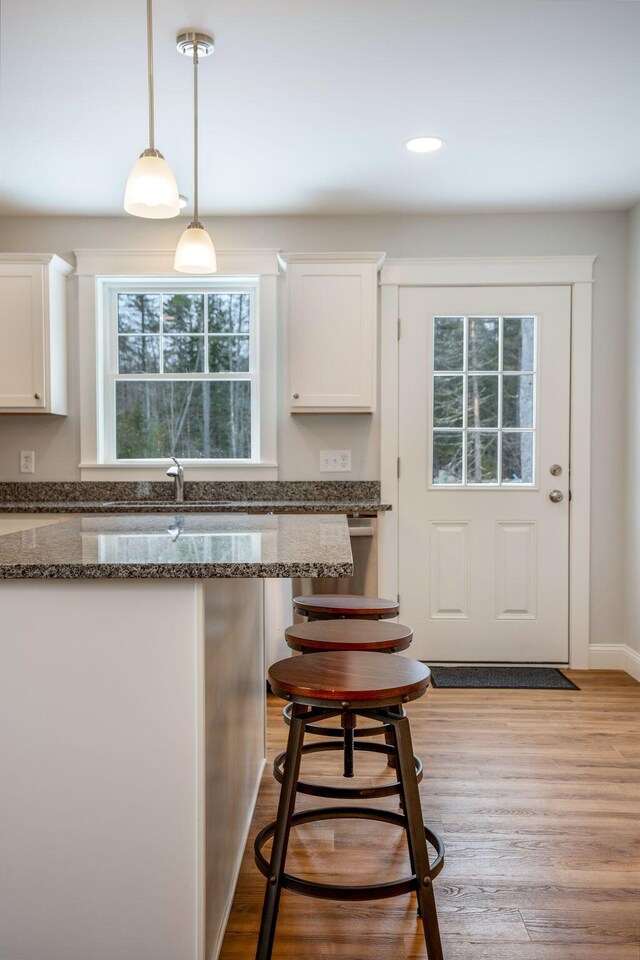 kitchen featuring a kitchen breakfast bar, light hardwood / wood-style flooring, hanging light fixtures, white cabinetry, and dark stone countertops