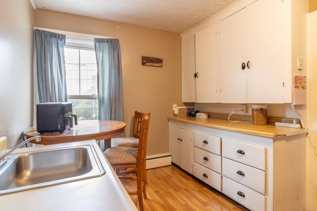 kitchen featuring baseboard heating, white cabinetry, light hardwood / wood-style floors, sink, and a textured ceiling