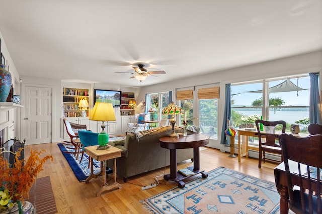 living room featuring ceiling fan, light wood-type flooring, and built in shelves