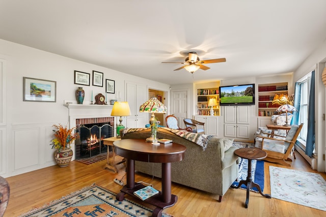 living room with a fireplace, light hardwood / wood-style flooring, built in shelves, and ceiling fan