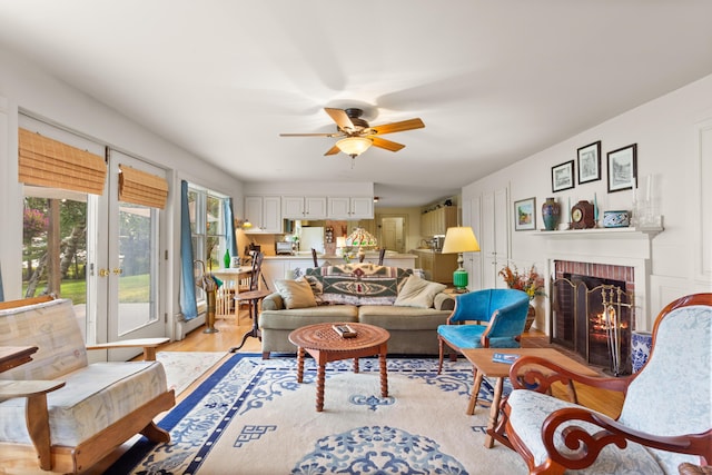 living room featuring light wood-type flooring, french doors, a brick fireplace, and ceiling fan