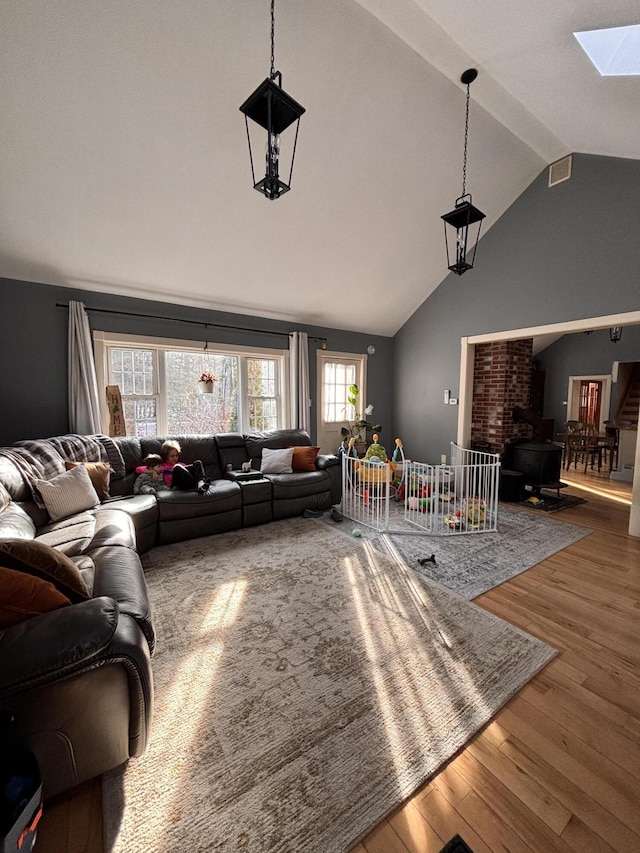 living room featuring lofted ceiling with skylight, hardwood / wood-style floors, and a wood stove