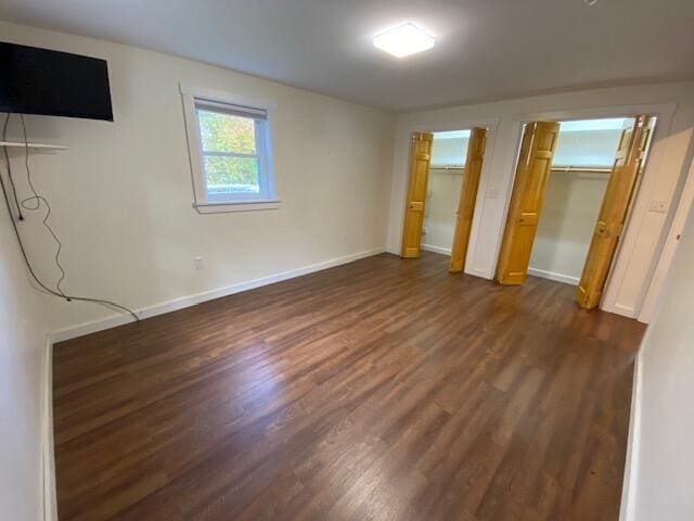 unfurnished bedroom with dark hardwood / wood-style flooring and multiple closets