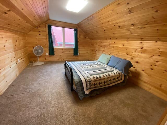 carpeted bedroom with wooden ceiling, wood walls, and lofted ceiling