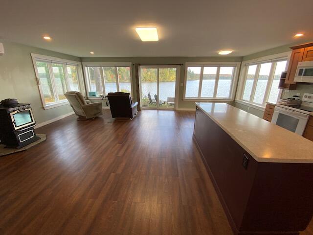 interior space with white appliances, a water view, a center island, dark hardwood / wood-style floors, and a wood stove