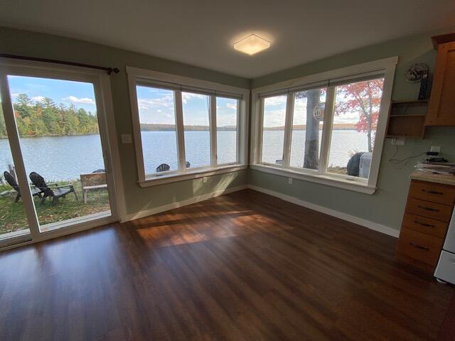 unfurnished dining area featuring a healthy amount of sunlight, a water view, and dark hardwood / wood-style flooring