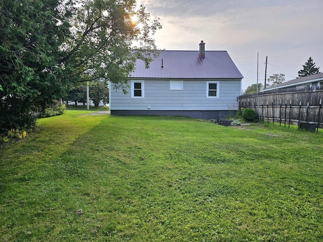 rear view of property with a chimney, fence, metal roof, and a lawn