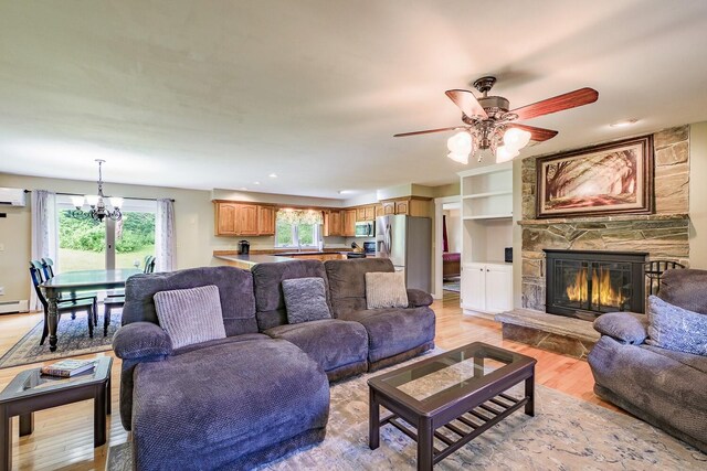 living room featuring built in shelves, ceiling fan with notable chandelier, light hardwood / wood-style floors, a fireplace, and a wall mounted air conditioner