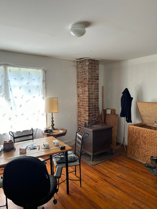 home office featuring a wood stove, hardwood / wood-style flooring, and brick wall