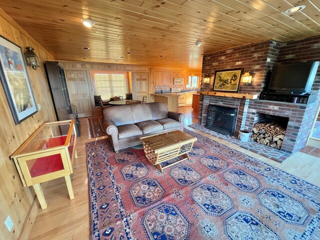 living room featuring a brick fireplace, light hardwood / wood-style floors, wood walls, wooden ceiling, and brick wall