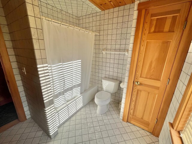 bathroom with tile walls, shower / tub combo with curtain, tile patterned flooring, and toilet