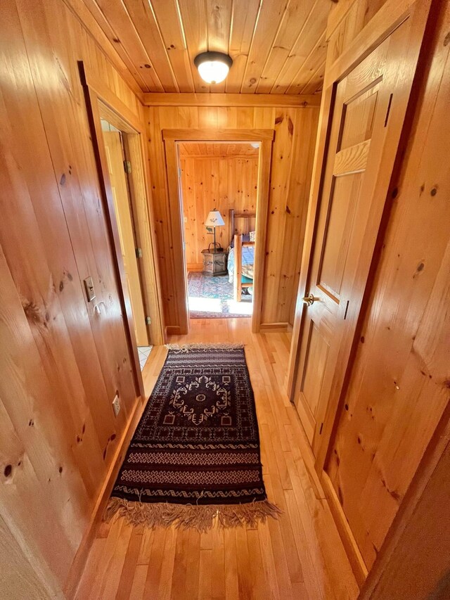 hall with light hardwood / wood-style flooring, wood walls, and wood ceiling