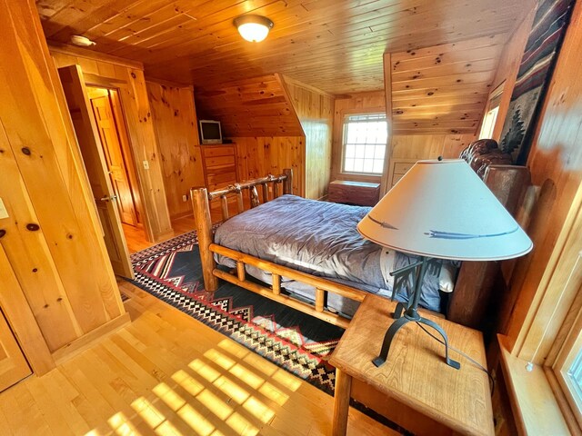 bedroom with wooden walls, wood ceiling, vaulted ceiling, and light hardwood / wood-style floors